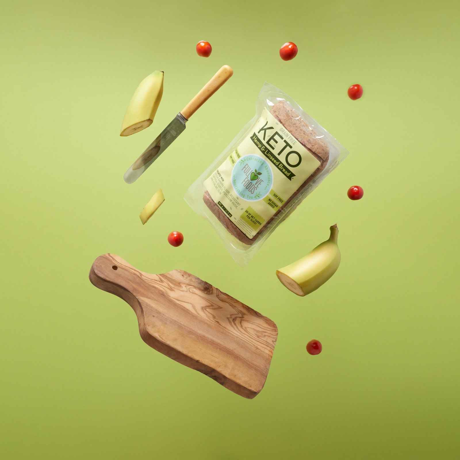 Floating keto bread with bananas, tomatoes, and chopping board on green background.